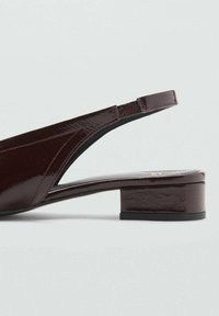 Burgundy patent leather slingback shoe with a low block heel, pointed toe, and elastic strap for secure fit. Smooth, glossy finish.