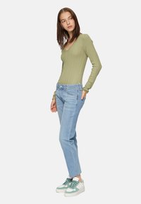 Hellgrünes, geripptes Langarmoberteil kombiniert mit hellblauen Jeans im geraden Schnitt und weißen Sneakers mit grünen Akzenten. Einfaches und modernes Design.