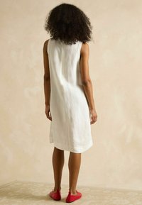 Weißen Leinen ärmelloses Kleid, das knapp über dem Knie endet, kombiniert mit roten Ballerinas. Einfaches, minimalistisches Design mit geradem Schnitt.