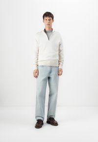 Weißer Viertelreißverschluss-Sweatshirt mit gerippten Bündchen, hellblaue gerade Jeans und dunkelbraune Schnürschuhe, in einem minimalistischen Umfeld.