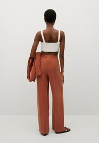 Biały crop top, szerokie, rdzawoczerwone spodnie z elastycznym paskiem w talii oraz pasująca, oversize'owa kurtka trzymana w dłoniach. Gładki materiał i luźny krój.