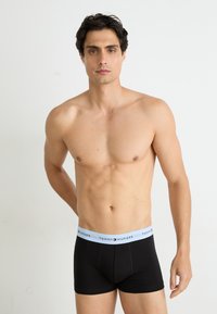 Fekete boxer alsónadrág világoskék elasztikus derékkal, amelyen a "Tommy Hilfiger" logó szerepel; puha anyagú, szabott fazon, sima textúrájú.