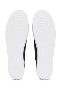 Paire de chaussures noires retournées, montrant les semelles extérieures en caoutchouc blanc avec une semelle texturée et le logo "Tommy Hilfiger".