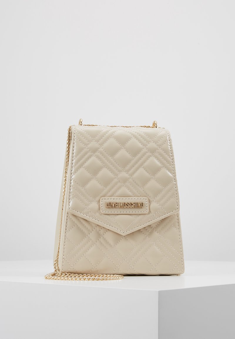 Borsa a tracolla in finta pelle trapuntata beige con una tracolla in metallo dorato, un flap frontale e una placca con logo. Testurizzata con motivi a diamante.