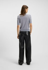 Maglione azzurro chiaro a maniche corte realizzato in un tessuto morbido, abbinato a pantaloni larghi in pelle nera a vita alta. Texture liscia e vestibilità rilassata.