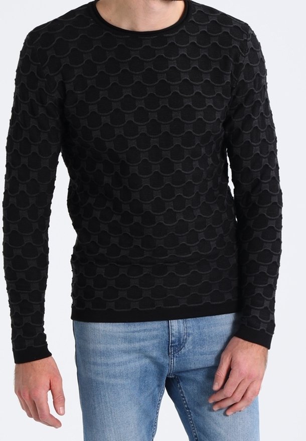 Pull noir à manches longues avec un motif texturé en vagues. Poignets et encolure côtelés, associé à un jean bleu clair.