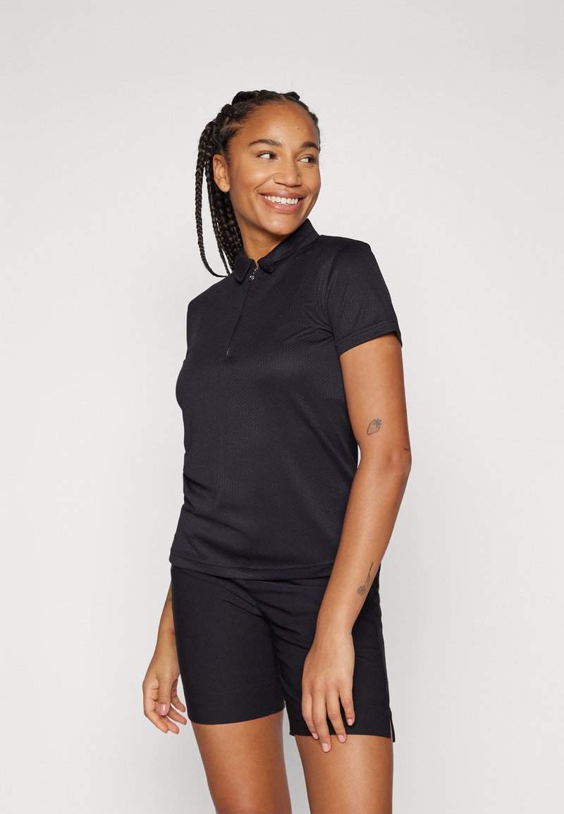 Črna polo majica s ovratnikom, kratkimi rokavi, teksturirano tkanino in zadrgo. Ujemajoče se črne kratke hlače.