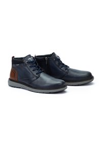 Botas de tobillo para hombre en cuero azul marino oscuro con acentos marrones, que cuentan con cordones, una cremallera lateral y una suela de goma. Textura suave y forma redondeada.