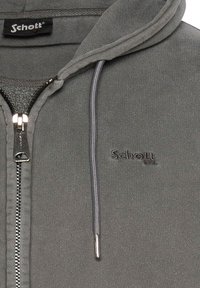 Grå zip-up hættetrøje lavet af blødt stof, med snørerhætte og broderet "Schott" logo på venstre bryst. Sølvfarvet lynlås.