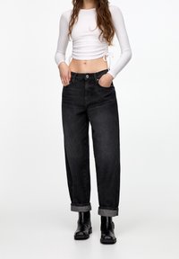 Jeans noirs taille haute à coupe décontractée, ourlets retroussés et poches avant, associés à un crop top blanc à manches longues.