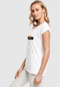 Weißes Baumwoll-T-Shirt mit aufgerollten Ärmeln, mit schwarzem und orangefarbenem "MOM"-Text und einer Kronen-Grafik, lockere Passform, glatte Textur.