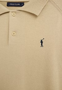 Beiges Poloshirt mit zwei Knöpfen, geripptem Kragen und einem kleinen, dunkelblau bestickten Golfer-Logo auf der linken Brust.