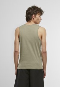 Olivengrünes, leichtes Baumwoll-Tanktops mit rundem Ausschnitt, ärmellosem Design und lockerer Passform, getragen mit schwarzen Shorts.