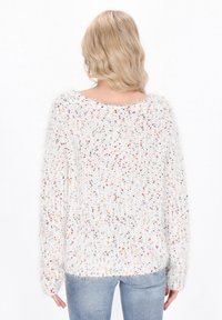 Flauschiger weißer Pullover mit mehrfarbigen Sprenkeln, weitem Ausschnitt und langen Ärmeln. Weiche Textur mit lockerer Passform, an der Rückseite etwas länger.