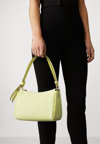 Bolso de mano de cuero amarillo con un detalle trenzado, con una doble correa en amarillo y negro. Textura lisa con un cierre de cremallera.