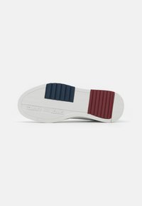 Biała podeszwa sneakersów z niebieskimi i czerwonymi akcentami z gumy. Posiada żłobioną teksturę oraz wytłoczone logo "TOMMY JEANS" z boku.