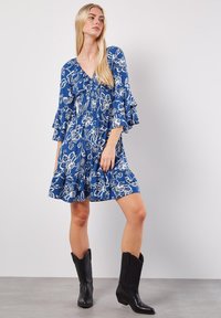 Blå blommig klänning med volangärmar, med djup V-ringning och knälång fåll. Bärs med svarta cowboykängor, vilket framhäver kontrasten i outfiten.