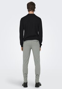 Suéter de punto negro de manga larga, pantalones grises claros ajustados con bolsillos traseros y zapatos negros. Diseño simple y ajustado sin patrones visibles.