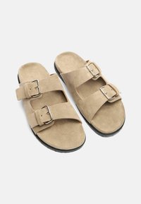 Tan nubuck sandaaltjes met twee verstelbare riemen en zilveren gespen. Gecorrigeerde voetbed en zwarte rubberen zool voor comfort en stabiliteit.