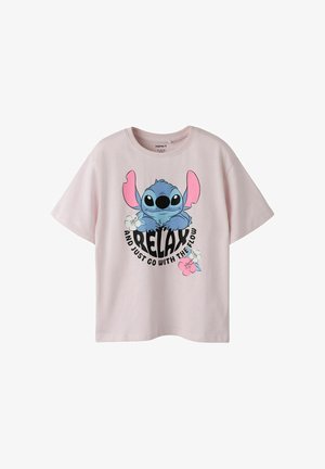 T-shirt rose clair avec un personnage extraterrestre bleu cartoon, des fleurs et le texte « RELAX and just go with the flow » sur le devant.