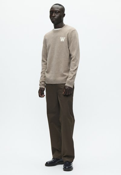Pull texturé marron clair avec logo "W" sur la poitrine, associé à un pantalon large vert olive foncé et des chaussures noires, sur fond blanc.