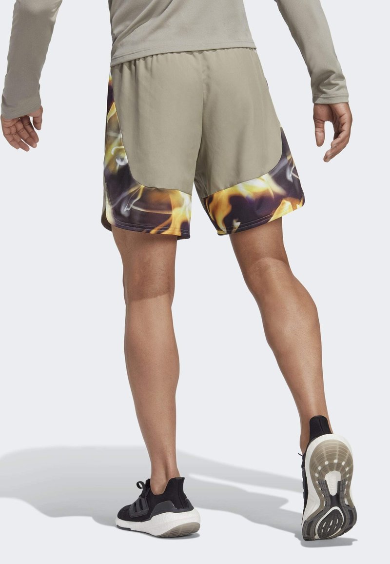 Pantalones cortos deportivos para hombres en gris claro con un dobladillo con diseño de llamas. Presentan una tela suave y una cintura elástica. Combínalos con zapatillas negras.