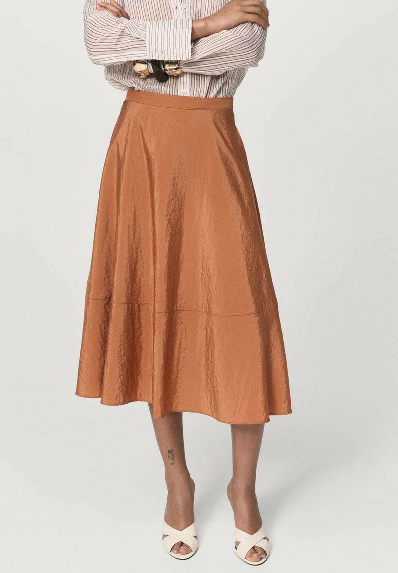 Een middellange A-lijn rok van textuurstof in roestkleur, met een gladde tailleband en een casual silhouet, gecombineerd met strappy witte schoenen.