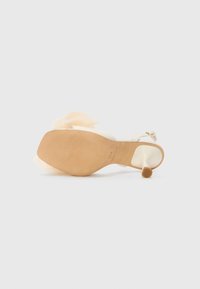 Høyhælte sandaler med overdel av beige lær, gjennomsiktig rem og lagdelt, lett stoffdekorasjon. Flat, glatt såle.