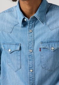 Vaaleansininen denimpaita painonapeilla, länsityylisellä yläosalla, kahdella rintataskulla ja pienellä punaisella Levi's-lipukkeella vasemmassa taskussa.