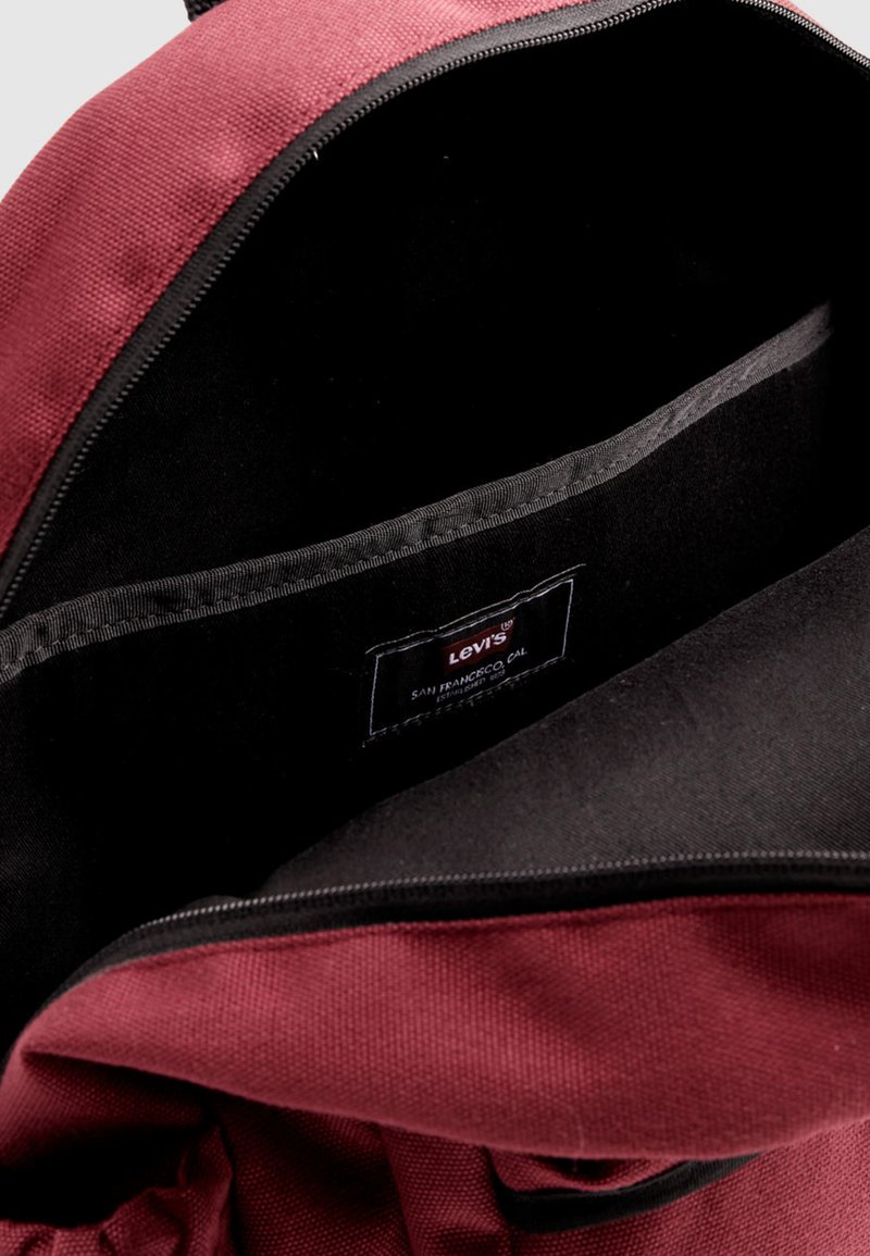 Intérieur d'un sac à dos en tissu marron avec doublure noire, affichant une étiquette indiquant "Levi's, San Francisco, Cal." et un bord de fermeture éclair lisse.