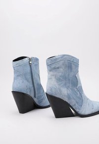 Botas de denim azul claro hasta el tobillo con un tacón negro afilado y cremallera lateral, que cuentan con un patrón de diseño cosido en la caña.