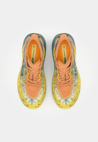 Zapatillas de running con un upper de patrón vibrante en amarillo y azul, acentos naranjas, un diseño de malla transpirable y suela texturizada.