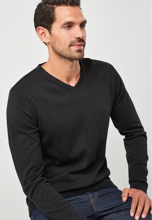 Sort langærmet V-hals sweater i en struktureret stof. Casual pasform med ribbede manchetter, parret med blå jeans.