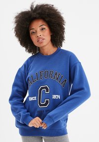 Sudadera azul de mezcla de algodón con cuello redondo acanalado. Presenta el texto "CALIFORNIA" y el logo "C" en blanco, un ajuste cómodo y mangas largas.