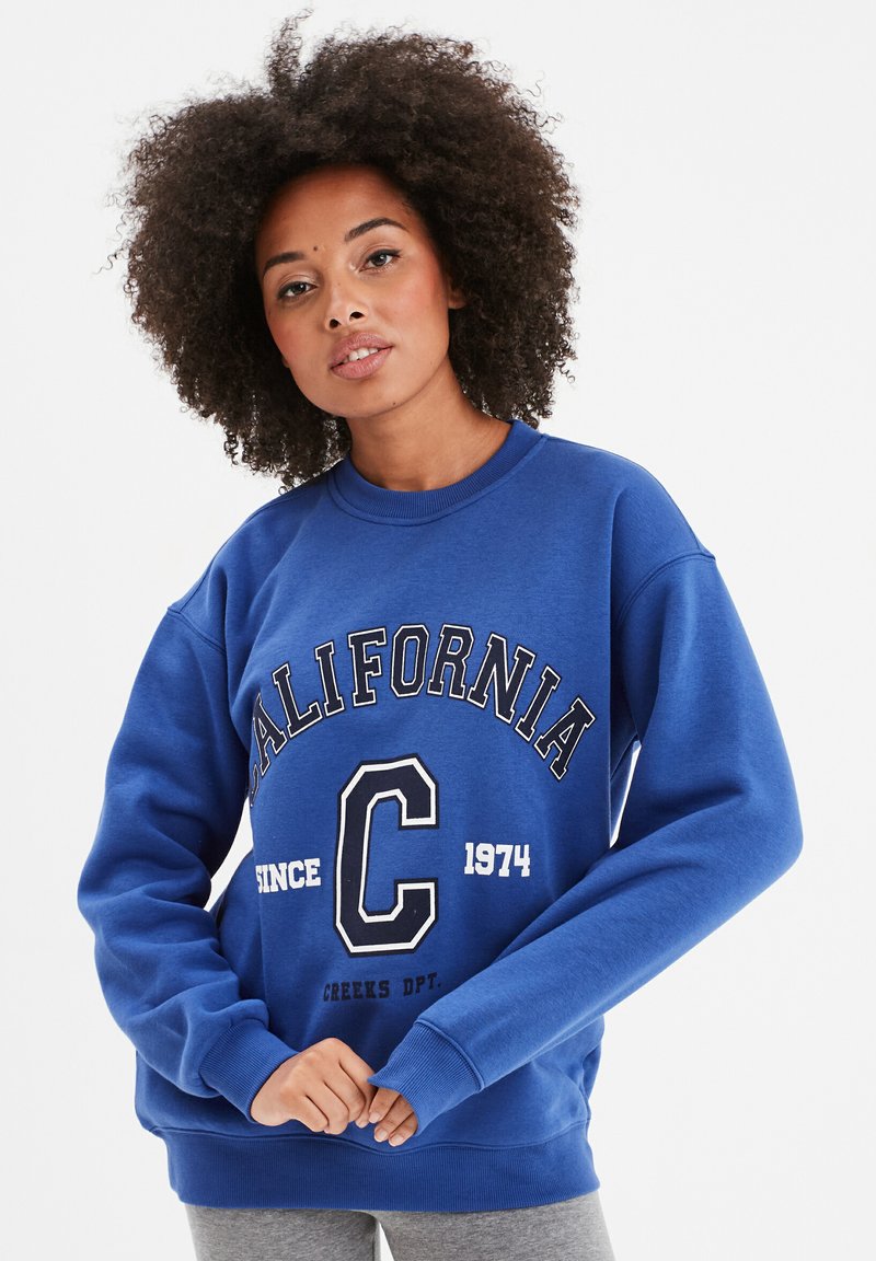 Sudadera azul de mezcla de algodón con cuello redondo acanalado. Presenta el texto "CALIFORNIA" y el logo "C" en blanco, un ajuste cómodo y mangas largas.
