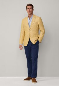 Blazer en lin jaune avec des revers, deux boutons, poches plaquées ; assorti à une chemise rayée bleu et blanche, un pantalon navy et des mocassins marron.