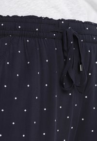 Mörkblå pyjamasbyxor, lättviktig textil, med vita prickar, elastisk midja med snörning och slät yta.