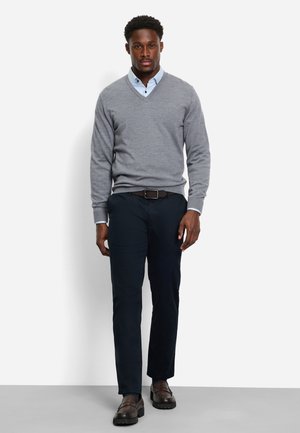 Grauer V-Ausschnitt-Pullover über einem hellblauen Hemd mit Kragen, kombiniert mit dunklen Hosen und braunen Schuhen. Glatte Textur, lässige Passform und schlichtes Design.