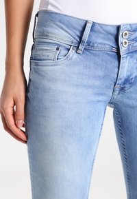 Ljusblå denimjeans har en svag gradient från mörkt till ljust. Tvåknapps stängning, framfickor och sömdetaljer är synliga.