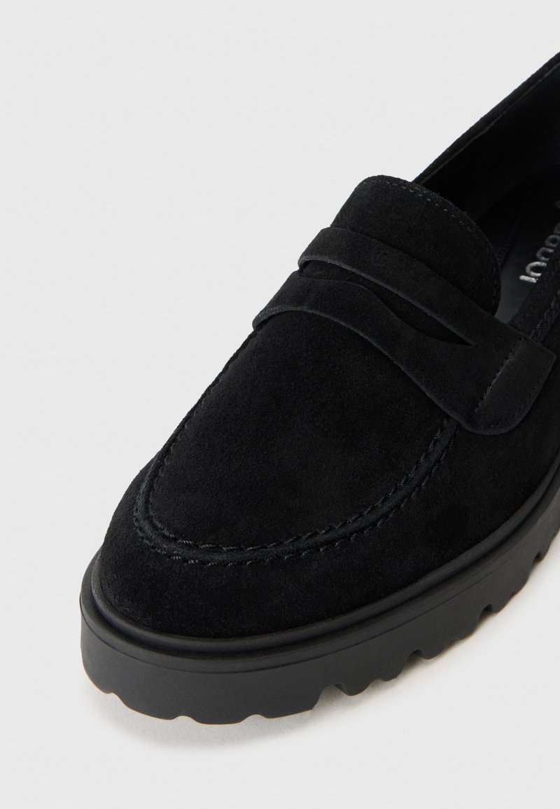 Close-up van een zwarte suède instapschoen met een decoratieve band en een gestructureerde rubberen zool, tegen een effen grijze achtergrond.