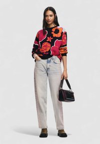 Maglione colorato con motivo floreale in tonalità di rosa e nero, abbinato a jeans in denim chiaro con design a gradiente e borsa nera.
