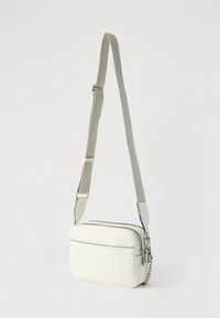 Bijela teksturirana torbica na rame s patentnim zatvaračem na vrhu, podesivim remenom i srebrnim ukrasima. Ima diskretan uzorak s logotipom.