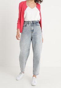 Light blue high-waisted jeans with a relaxed fit, paired with a white tank top and a pink cardigan. White sneakers complete the outfit.