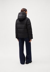 Black puffer jacket with a hood, featuring a quilted design and oversized fit, paired with wide-leg jeans and chunky black boots.
