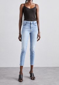 Top de tirantes oscuro con canalé, combinado con unos pantalones vaqueros recortados de color azul claro. Presenta una silueta ajustada y un ligero desvanecimiento. Se lleva con tacones negros de punta abierta.