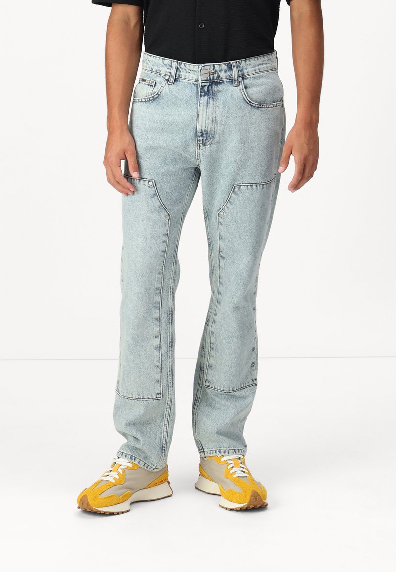 Jeans en denim bleu clair avec une coupe décontractée, dotés de poches à rabat, de coutures visibles et d'une conception à jambe droite.