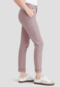 Rosa avsmalnande byxor med sidofickor, uppvikta slut och en slät yta, tillsammans med vita sneakers med gråa detaljer.