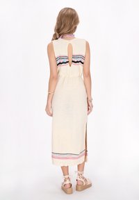 Rochie tricotată în crem, cu un bandou brodat multicolor, tăietură pe spate, fanta laterală și tiv ondulat. Pur și simplu asortată cu espadrile cu sfori.