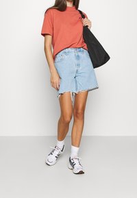 Bawełniany t-shirt w kolorze rdzy, wysokie szorty dżinsowe, białe trampki z czarnymi akcentami oraz czarna torba typu tote o matowym wykończeniu.