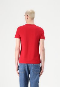 Camiseta corta roja de algodón, con un clásico cuello redondo y un diseño ajustado. Se lleva con unos vaqueros de mezclilla azules.